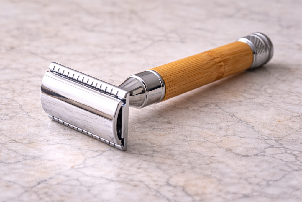 Close-up of a chrome safety razor with a bamboo handle resting on a light marble surface, showing a reusable shaving tool designed to replace disposable plastic razors.