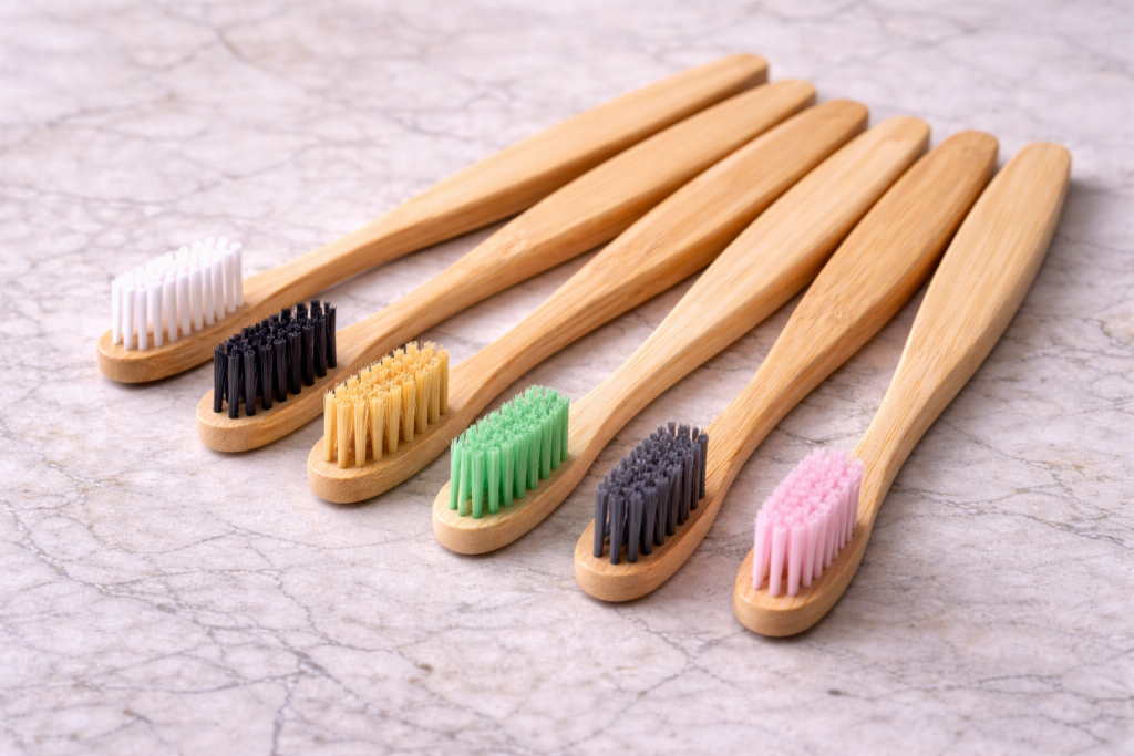 Row of six bamboo toothbrushes with different colored bristles displayed on a marble surface, representing eco-friendly alternatives to plastic toothbrushes.