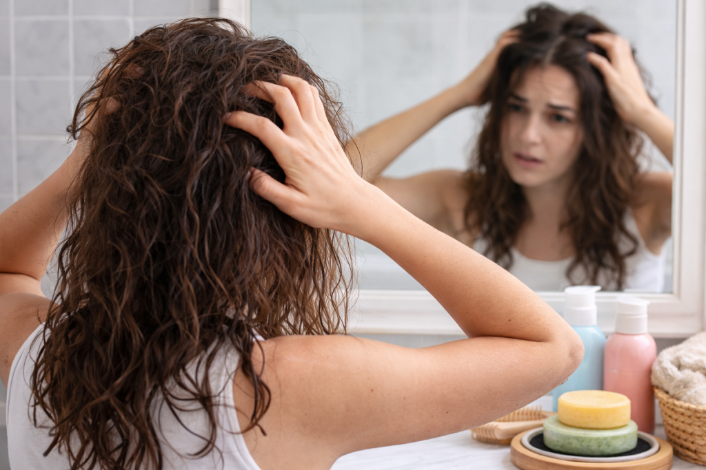 Woman examining her hair in a bathroom mirror during the shampoo bar transition period, representing the adjustment phase when switching from liquid shampoo to plastic-free shampoo bars.